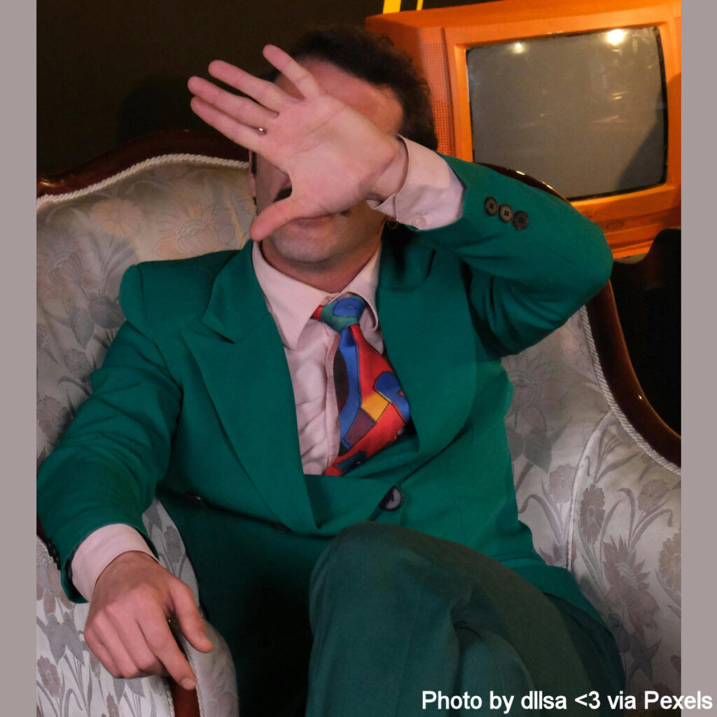 Man in an awful green suit blocking out the viewer with an upraised hand